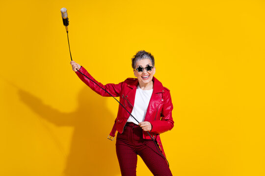 Colorful woman celebrating with microphone and stylish red outfit against vibrant yellow background