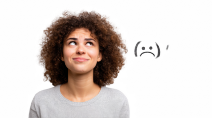 Young woman with curly hair wearing casual grey outfit looking up with pensive expression and a hand drawn sad face above her, isolated on transparent background