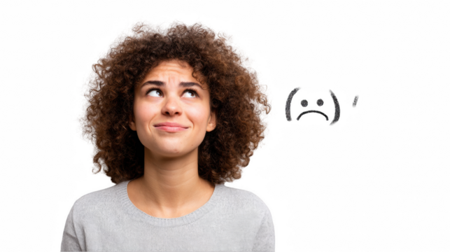 Young woman with curly hair wearing casual grey outfit looking up with pensive expression and a hand drawn sad face above her, isolated on transparent background