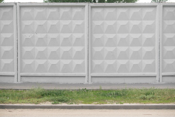 Textured concrete wall with geometric patterns, featuring a smooth gray surface and grassy area below, creating a modern urban aesthetic with copy space for design