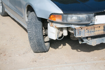 Close-up view of a damaged car front with a visible tire and exposed mechanical parts, showcasing wear and tear in an outdoor environment with natural lighting