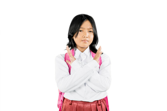Fototapeta Asian schoolgirl making X sign with arms, expressing refusal or protest, wearing uniform and backpack on white background