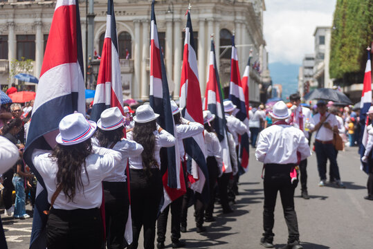 A group of students carrying Costa Rican flags march in a patriotic Independence Day parade in a historic city center. 