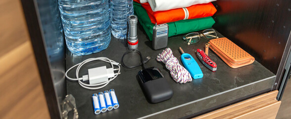 Banner of 72 hour survival kit in kitchen cupboard with water bottles, clothes, radio, batteries, powerbank, flashlight, knife and lighter. Full pantry ready for disasters, war, pandemic or blackout.