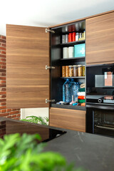 Cupboard with canned food, water bottles, first aid supplies and clothes in modern kitchen. Survival pantry stored according to government recommendations about emergency or war preparedness.