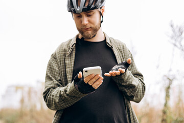 Man cyclist standing in a field using smartphone. Concept of outdoor technology.
