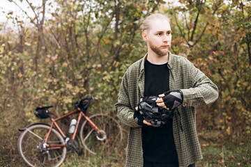 Young bearded man in casual clothes putting on protective bike helmet.