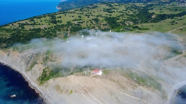 Aerial panoramic view of Cape Emine on the Bulgarian Black Sea coast. Dramatic cliffs, a historic lighthouse, and turquoise waters shrouded in mysterious sea mist, captured by drone.