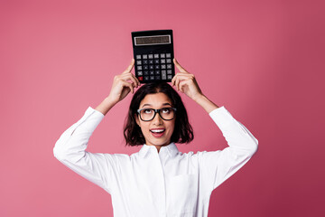 Confident young woman holding calculator above her head on vibrant pink background, symbolizing intelligence and creativity