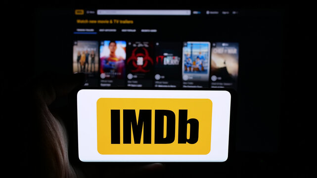 Stuttgart, Germany - 05-27-2025: Person holding cellphone with logo of US platform Internet Movie Database (IMDb) on screen in front of webpage. Focus on phone display.