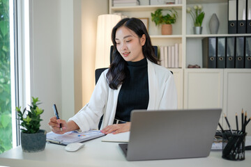Professional woman working at office desk analyzing financial charts and graphs with laptop and documents.