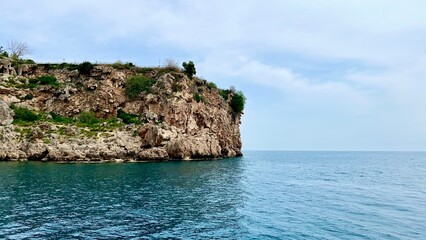 Fototapeta premium Turquoise sea with rocky cliff view. Summer vacation, Mediterranean Sea, travel, coastal landscape, nature, Antalya province, Turkey, outdoor scenery, peaceful summer day.