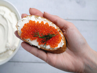A hand presents a piece of bread adorned with cream cheese and caviar, highlighting a luxurious culinary treat.