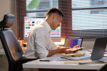 Graphic designer concentrating on visual design tasks, surrounded by digital tools, and warm ambient lighting.