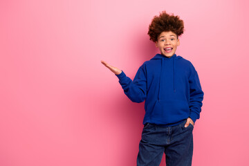 Cheerful boy in a blue hoodie posing with a delighted expression on a vibrant pink background...