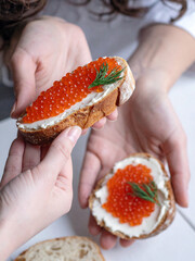 One person is handing another person two slices of bread with cream cheese and red caviar, presenting an exquisite appetizer.