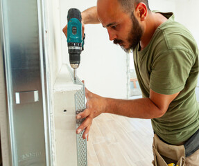 Construction worker installing metal corner bead on drywall with cordless screwdriver