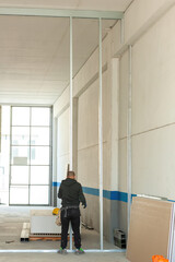 Construction worker installing aluminum pillars for plasterboard wall in industrial building