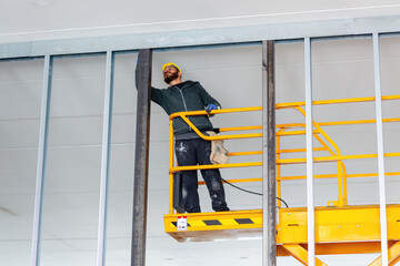 Construction worker installing drywall on a mobile elevating work platform