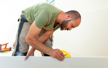 Construction worker sanding drywall with hand sander during home renovation