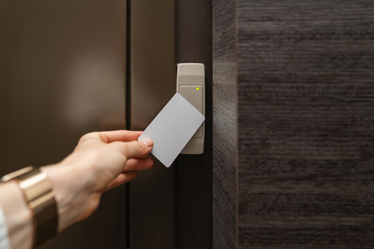 Close-up of person's hand holding a white access card near a key reader access device next to the locked door. Green light indicates access granted. Security, smart access management, entry technology