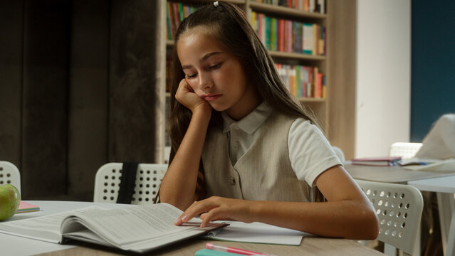 Bored schoolgirl Caucasian girl kid child pupil read book in school library sad tired learner student teenager upset frustrated boring lesson exhausted sleepy reading studying in classroom education