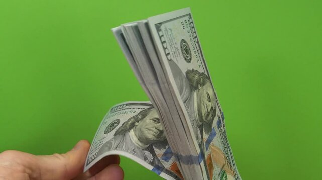 Man checks a wad of hundred dollar bills. Cash counting. Converting cash American dollars. Hands holds banknotes at green background. Man holds hundred dollar bills in hands. New hundred dollar bills