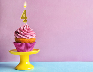 Yummy cupcake with burning golden candle in shape of number 4 on table against violet background,...