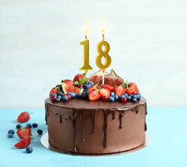 Yummy chocolate cake with fruits and burning number shaped candles on light blue table. 18th...