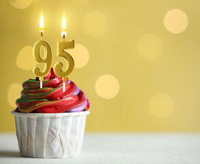Yummy cupcake with burning number shaped candles on yellow background with blurred lights, space for text. 95th birthday or other special occasion