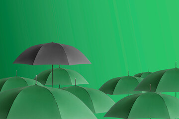 Black umbrella among green ones against color background