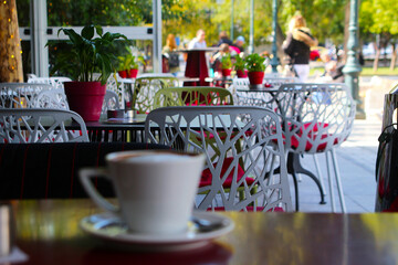 Outdoor coffee house scene with selective focus on chairs and cappuccino cup in bokeh