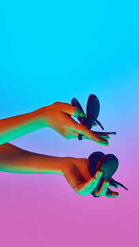 Pair of hands rhythmically moving castanets under blue and purple neon light against gradient studio background. Concept of music sound, percussion art and cultural music tradition.