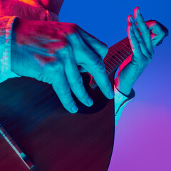 Extremely close-up on musician's hands playing mandolin under colorful neon light against...