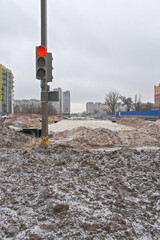 Construction of an asphalt road in winter among high-rise buildings near a traffic light that shines red