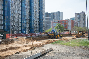 construction of a road near a large multi-storey residential building using two tractors with large iron buckets
