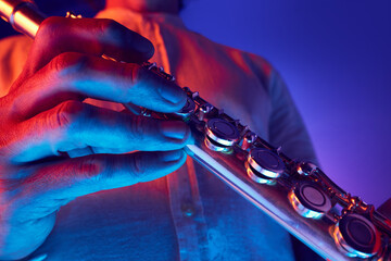 Male musician holding and playing flute with focused hand detail under colored lighting against...