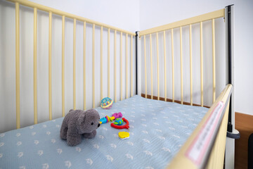 An empty hospital bed, designed for infants or young children, features light rails, a patterned mattress, and toys, set in a sterile room.