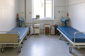 An intensive care ward, for respiratory patients, features two empty beds, oxygen concentrators, a cardiograph, ventilators, and IV stands in a sterile room.