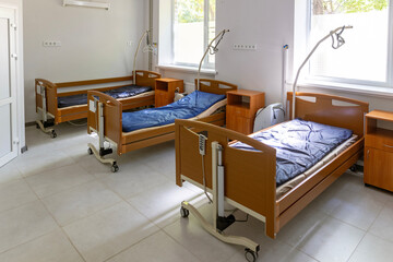 A multi-bed hospital ward features three empty beds, each with a lung ventilator, oxygen concentrator, and oxygen hub, in a brightly lit, sterile environment.
