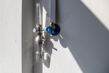 An oxygen flow meter with a humidifier bottle is mounted on a white wall, part of an oxygen hub, ready for use in a hospital intensive care unit.