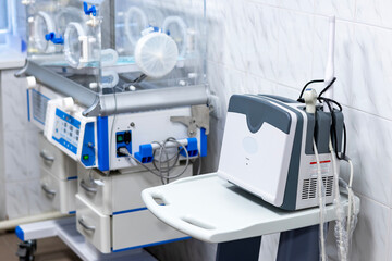 A medical room features a transparent infant incubator and a portable ultrasound device on a mobile cart, showcasing advanced healthcare equipment.