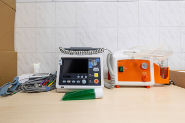 A new, unplugged defibrillator monitor with pacing mode and a portable suction pump sit on a wooden table in a hospital room.