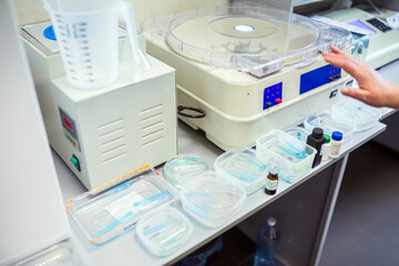 Laboratory equipment including a centrifuge, measuring cup, and various medical supplies like test tubes and vials are arranged on a workbench.