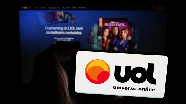 Stuttgart, Germany - 05-27-2025: Person holding mobile phone with logo of Brazilian web platform Universo Online (UOL) on screen in front of web page. Focus on phone display.