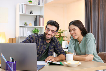 Business couple working, communicating while sitting at the home office desk together. Cheerful couple, calm asian woman and caucasian man working at home with laptop together.