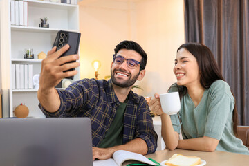 Business couple working, communicating while sitting at the home office desk together. Cheerful couple, calm asian woman and caucasian man working at home with laptop together.