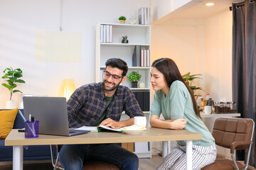 Business couple working, communicating while sitting at the home office desk together. Cheerful couple, calm asian woman and caucasian man working at home with laptop together.