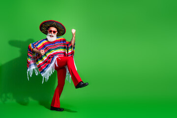 Charismatic elderly man in colorful Mexican attire enthusiastically dancing against vibrant green background
