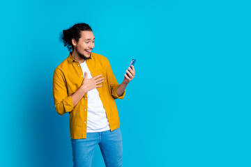 Young man in yellow shirt enthusiastically using smartphone against vibrant blue background for...